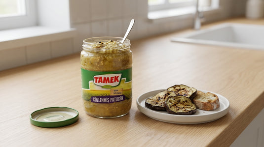 Bocal d'aubergines grillées TAMEK ouvert avec quelques tranches égouttées et une tartine de pain grillé, sur un plan de travail en bois clair