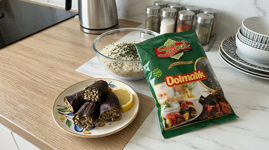 Aubergines séchées SIBEL réhydratées et farcies de riz, servies sur une assiette avec un quartier de citron, à côté du paquet de dolmalık aubergines séchées SIBEL et d'un bol de riz