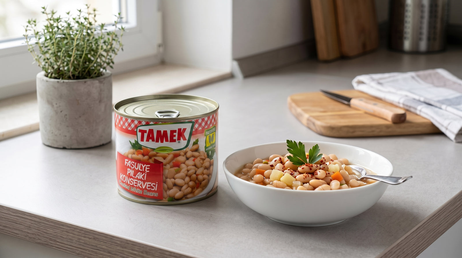 Bol de fasulye pilaki (haricots blancs, carotte, pomme de terre) à côté de la boîte TAMEK sur un plan de travail de cuisine moderne
