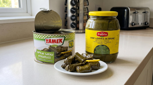 Boîte ouverte de feuilles de vigne farcies TAMEK avec quelques dolmas sur une assiette, à côté d'un bocal de feuilles de vigne nature PALIRA, sur un plan de travail de cuisine moderne