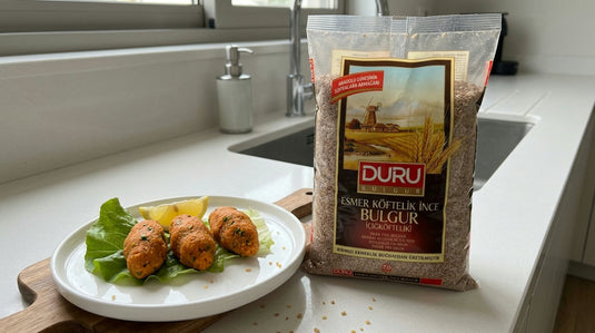 Assiette de boulettes de mercimek köftesi façonnées à la main, posées sur des feuilles de salade avec des quartiers de citron, à côté d'un paquet de boulgour fin DURU