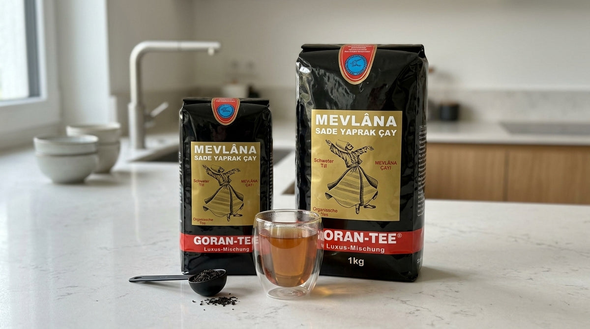 Paquets de thé noir MEVLANA Goran-Tee en vrac, format 500g et 1kg, posés côte à côte sur un plan de travail avec un verre de thé