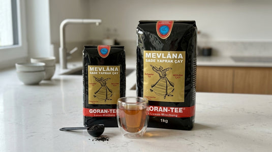 Paquets de thé noir MEVLANA Goran-Tee en vrac, format 500g et 1kg, posés côte à côte sur un plan de travail avec un verre de thé