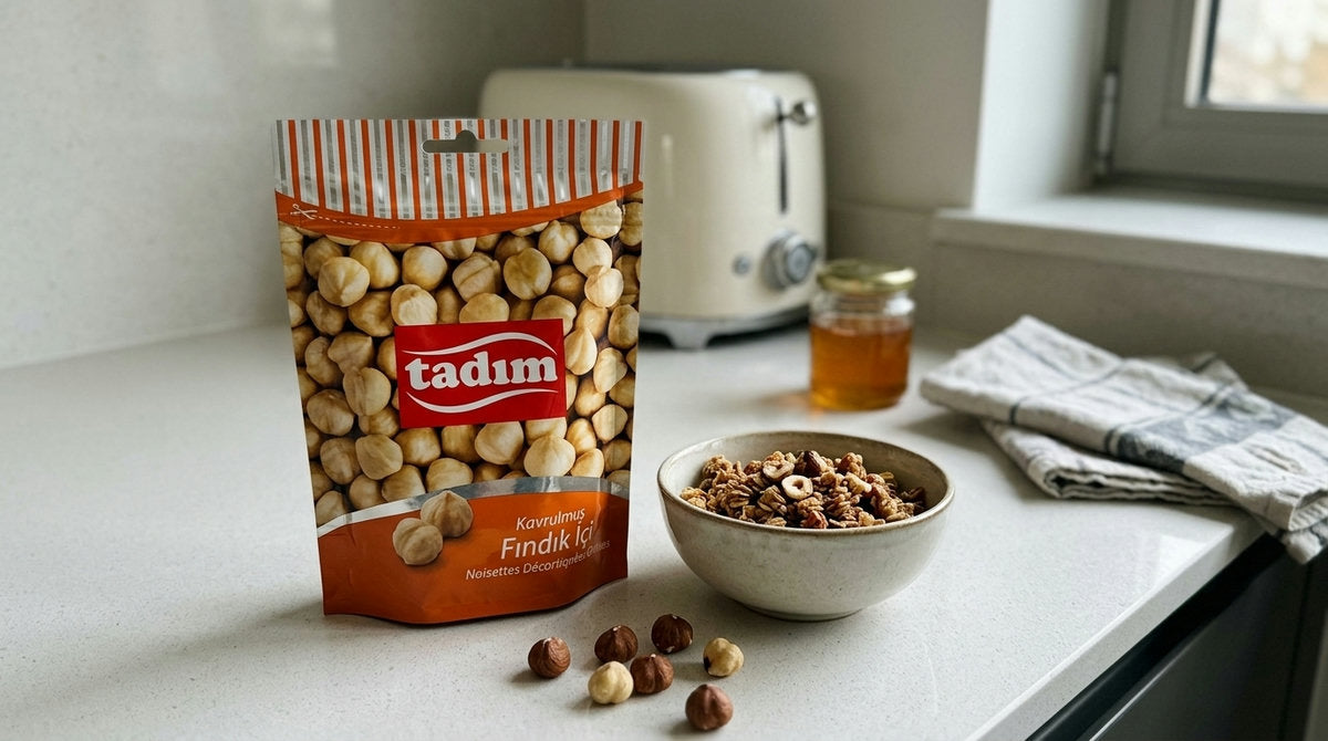 Sachet de Noisettes Décortiquées Grillées TADIM à côté d'un bol de granola maison parsemé de noisettes concassées, sur un plan de travail de cuisine moderne