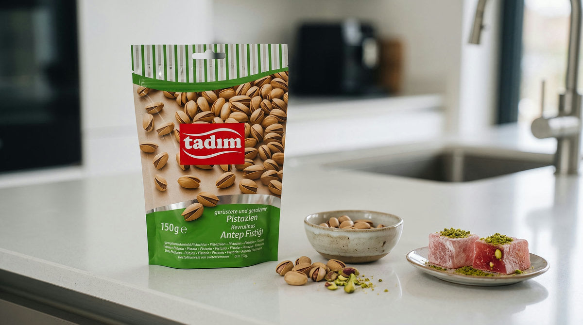 Sachet de Pistaches Grillées et Salées TADIM à côté d'un loukoum et d'un bol de riz pilaf parsemés d'éclats de pistache, sur un plan de travail de cuisine moderne
