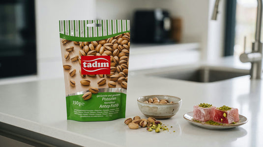 Sachet de Pistaches Grillées et Salées TADIM à côté d'un loukoum et d'un bol de riz pilaf parsemés d'éclats de pistache, sur un plan de travail de cuisine moderne