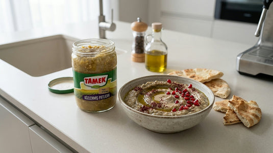 Bocal d'aubergines grillées TAMEK à côté d'un bol de tartinade façon babaganoush garnie de grenade et de sumac, avec du pain pita