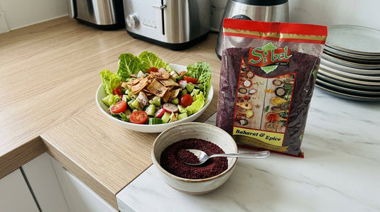 Bol de sumac moulu SIBEL avec une cuillère, à côté d'une salade de type fattoush et du paquet de sumac SIBEL