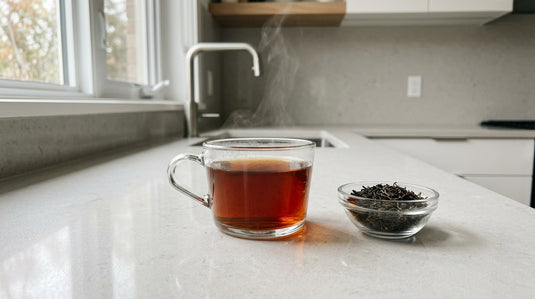 Tasse de thé noir fraîchement infusé posée à côté d'un bol de feuilles de thé en vrac, sur un plan de travail de cuisine moderne
