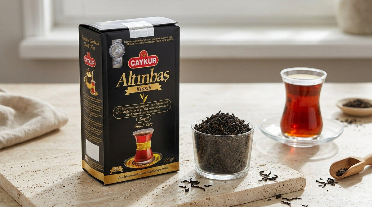 Paquet de thé noir ALTINBAS CAYKUR posé à côté de deux bols de feuilles de thé en vrac et d'un verre à thé turc, sur un plan de travail de cuisine moderne