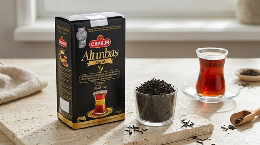 Paquet de thé noir ALTINBAS CAYKUR posé à côté de deux bols de feuilles de thé en vrac et d'un verre à thé turc, sur un plan de travail de cuisine moderne