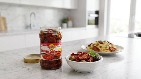 Bocal ouvert de tomates séchées SUNTAT à côté d'un bol de pâtes et d'olives sur un plan de travail de cuisine